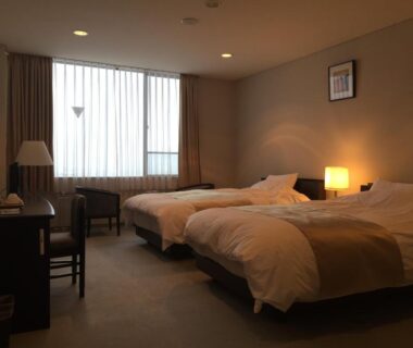 Twin beds with bedside lamps, desk and window curtains at Bekkan Yosanoso in Kyoto