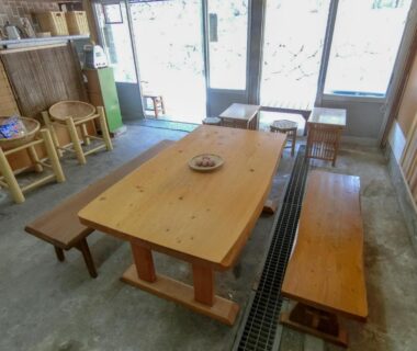 Low wooden communal table with benches and large windows at Beppu Kannawa Onsen HIROMIYA in Ōita