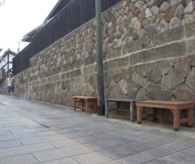 Stone wall with wooden benches along paved street near Beppu Kannawa Onsen HIROMIYA in Oita Kyushu