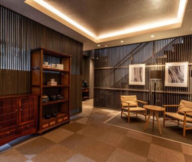 Warm-lit ryokan lobby with wooden slatted walls, chairs and decorative shelving at Beppu Nagomitsuki in Ōita