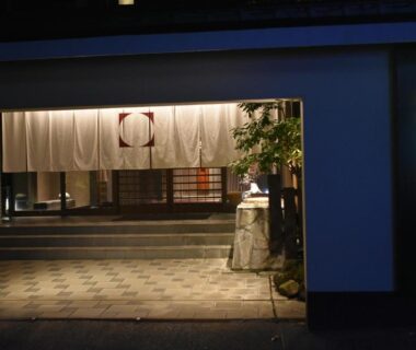 Noren curtain and lit sign at Beppu Nagomitsuki entrance in Ōita, tiled walkway and stone basin