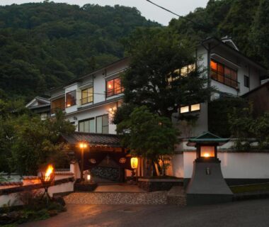 Dusk view of Beppu Showaen entrance with lit lanterns and hillside vegetation in Oita