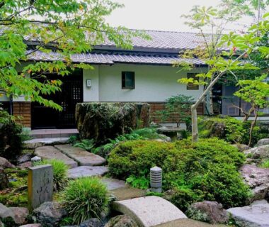 Stepping stone path through lush garden leading to traditional ryokan building at Beppu Showaen in Oita