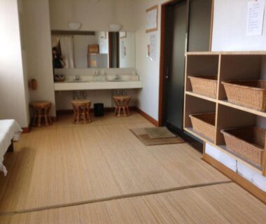 Tatami-floored changing area with wicker baskets, sinks and stools at Bergtour Marukita in Nagano