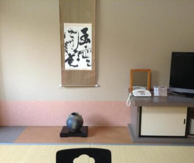 Tokonoma with calligraphy scroll, decorative vase, low cabinet and TV in Bergtour Marukita room, Nagano