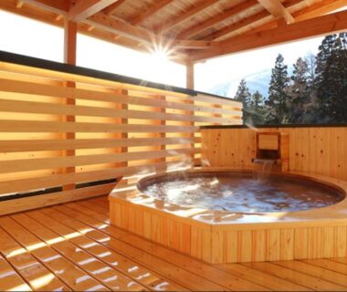 Circular wooden onsen bath on covered terrace at Bergtour Marukita with mountain and forest view in Nagano