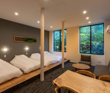 Spacious tatami room with futon bedding, low table and large windows overlooking greenery at Bessho Onsen Midoriya Nagano
