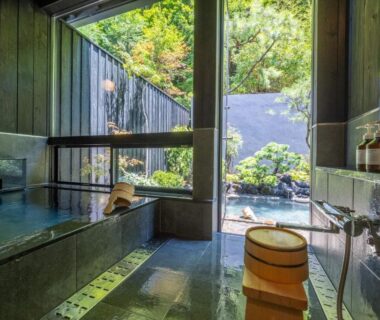 Indoor tiled onsen bathing area with wooden bucket and garden view at Bessho Onsen Midoriya Nagano