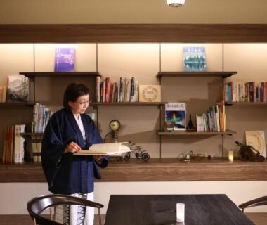 Guest in traditional robe reading in ryokan lounge with bookshelf and wooden counter