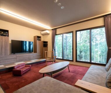 Bright lounge with low wooden table, sofa seating, TV console and floor-to-ceiling windows at Bettei Fujiya Hiroshima