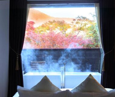 Low bed and pillows facing a steaming outdoor bath and autumn foliage at Bettei Koyoi in Kanagawa