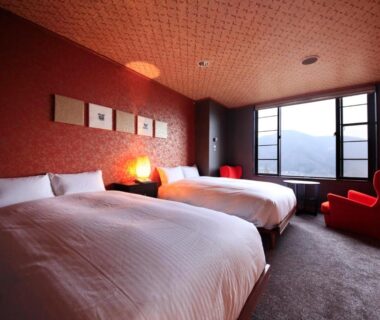 Two-bed room with red accent wall, armchair and window view at Bettei Koyoi, Kanagawa, Kantō