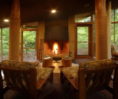 Lit fireplace with wooden armchairs and floor-to-ceiling windows overlooking lush forest at Bettei Senjyuan, Gunma