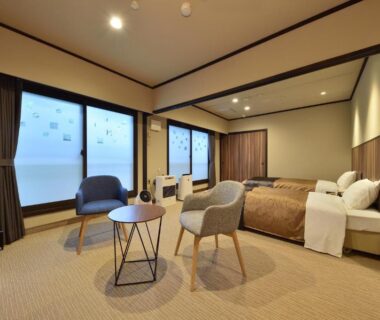 Modern guest room with two beds, lounge chairs, low table, and large frosted windows at Biei Shirogane Onsen AONOBI YUYU