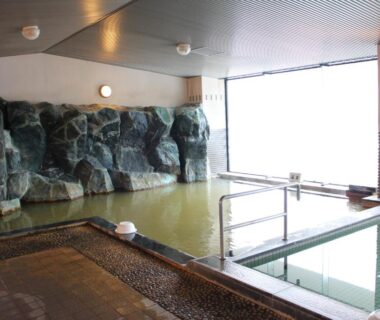 Spacious indoor onsen with rock feature, glass window and tiled bathing area at Biei Shirogane Onsen AONOBI YUYU Hokkaidō
