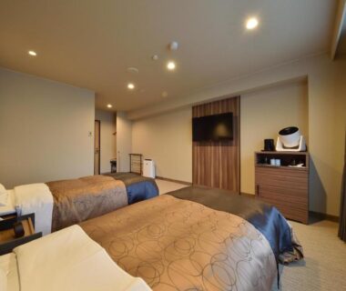 Spacious twin bedroom with carpet, two beds, bedside table, wall-mounted TV and window at Biei Shirogane Onsen AONOBI YUYU