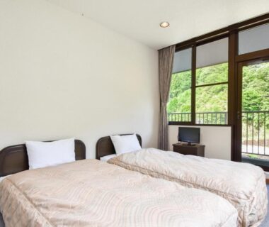 Twin beds with sliding glass doors opening to lush greenery outside at Bijintei in Wakayama
