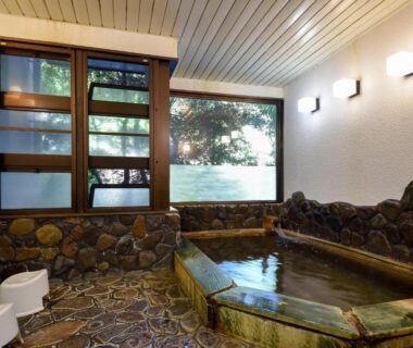 Indoor stone-lined bath with wooden-framed window and shower stools at Bijintei, Wakayama