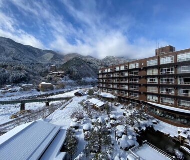 Snow-covered multi-story ryokan and courtyard at Bosenkan beside a river with mountains in Gifu, Chūbu, Japan