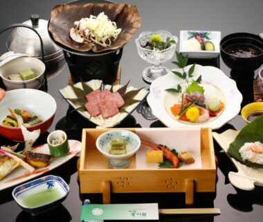 Assorted traditional Japanese dishes on lacquer table with sashimi, grilled meat, soup bowls and garnishes