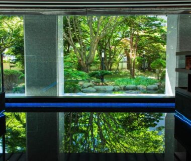 Reflective indoor bath with floor to ceiling window overlooking lush garden at Bourou Noguchi Hakodate in Hokkaido