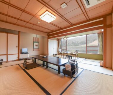 Spacious tatami room with low table and shoji screens, large window overlooking hills at Bousenkaku in Niigata, Chūbu, Japan