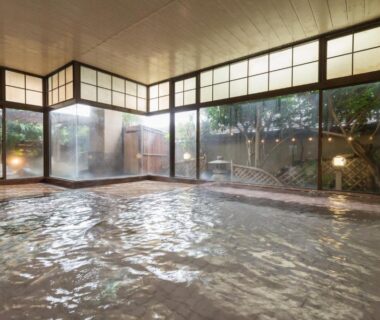 Spacious indoor onsen with wood-framed windows and garden beyond at Bousui in Shizuoka, Chūbu, Japan