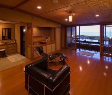 Spacious ryokan room with tatami area, wooden floors, leather chair and balcony overlooking the sea in Shizuoka