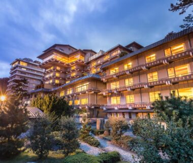 Dusk view of multi-story ryokan with lit balconies and landscaped garden paths, Bousui, Shizuoka