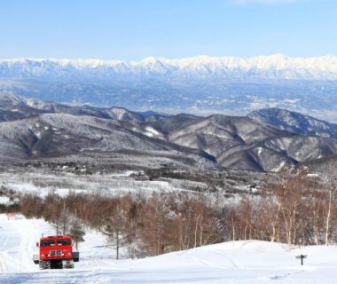Snow-covered ski slope with grooming vehicle and distant mountain range near Nagano Chūbu