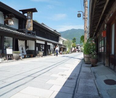 Stone-paved street flanked by wooden storefronts with distant mountain backdrop near Bouzantei Kotobuki, Nagano, Chūbu
