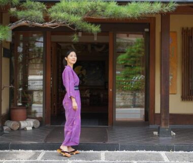 Woman in purple yukata standing at Bouzantei Kotobuki entrance in Nagano with wooden porch and potted plants