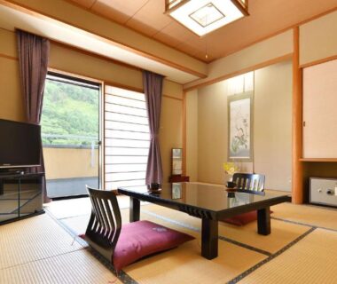 Traditional tatami room with low table, zabuton cushions, shoji screens and sliding door to green view at Bouzantei Kotobuki Nagano