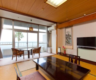 Tatami room with glossy low table, floor cushions, chairs by balcony railing and sea view at Boyokaku, Kumamoto