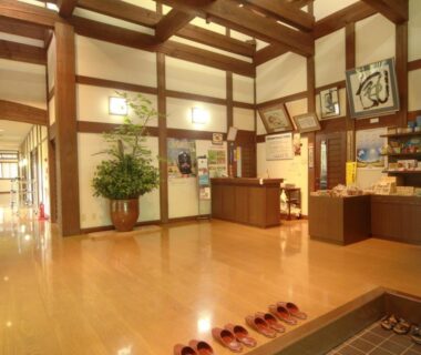 Spacious genkan entrance with lined slippers, wooden beams and reception desk at Bunanoyado Koase, Niigata