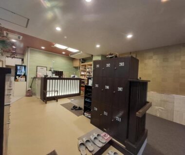 Genkan area with wooden shoe lockers, slippers, and reception counter at Business Ryokan Akashiya Annex in Hyōgo