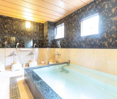 Communal bath with tiled soaking tub, shower stations, stools and windows at Business Ryokan Akashiya Annex