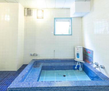 Indoor tiled communal bath with deep soaking section and small window at Business Ryokan Akashiya Annex in Hyōgo