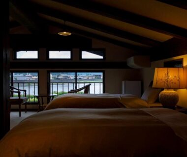 Two beds with bedside lamp, exposed wooden beams and balcony windows at Busuitei in Gifu Japan