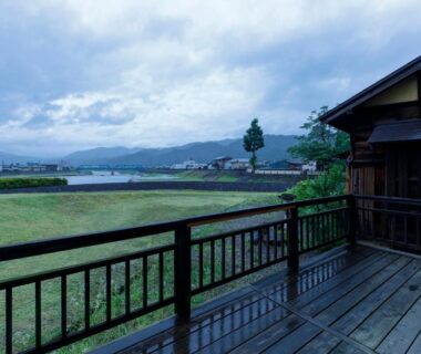 Wooden veranda and railing overlooking river, grassy bank and distant mountains at Busuitei in Gifu prefecture