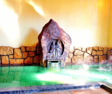 Steaming indoor onsen bath with stone wall and carved rock feature at Central Hotel in Nagano