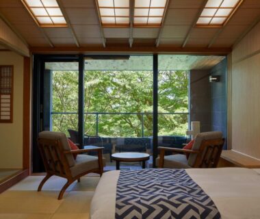 Tatami room with bed, two wooden chairs and large window overlooking green trees at Centurion Hakone Bettei, Kanagawa