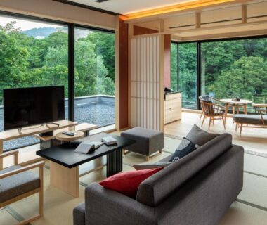 Spacious tatami lounge with sofa, low table, shoji screens and floor-to-ceiling windows overlooking forest at Chalet Ivy Jozankei
