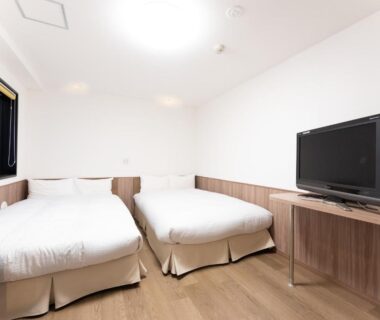 Compact twin room with wooden flooring, two beds and TV at Chang Tee Hotel Ikebukuro Tokyo
