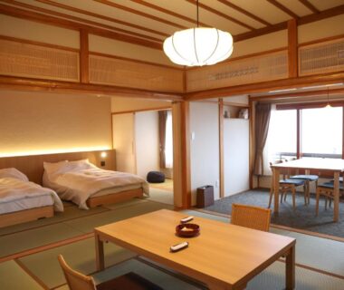 Spacious tatami room with twin beds, low wooden table and dining area at Chigira Jinsentei in Gunma