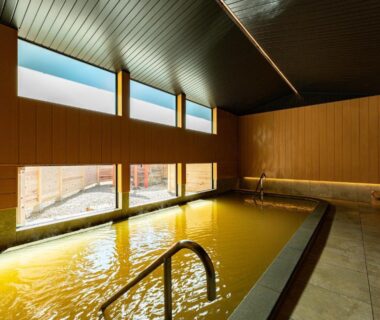 Indoor onsen with wooden interior, rectangular bath, metal handrail and high windows at Chigira Jinsentei, Gunma