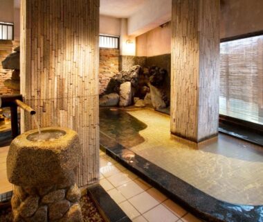 Indoor onsen bath with stone basin, bamboo pillars, tiled floor and rock feature at Chikurakan in Chiba