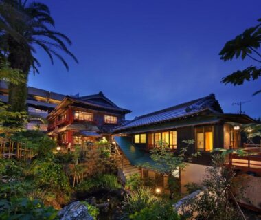 Nighttime exterior of Chikurakan with illuminated wooden buildings, lush garden and pond in Chiba, Kanto, Japan