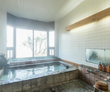 Indoor stone onsen bath with tiled walls, wooden buckets and large window at Chojuyu Hakone, Kanagawa