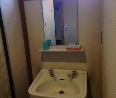 Small washbasin with two taps under mirror and shelf at Chuokan Shimizuya Ryokan Nagano
